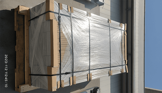 A photo of building panels stacked securely on a sturdy wooden pallet, tightly strapped, and wrapped in protective plastic film, ready for container loading.