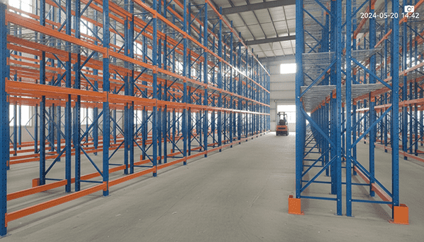 A clear, well-organized warehouse with pallet racking systems, showing forklifts operating in the aisles.