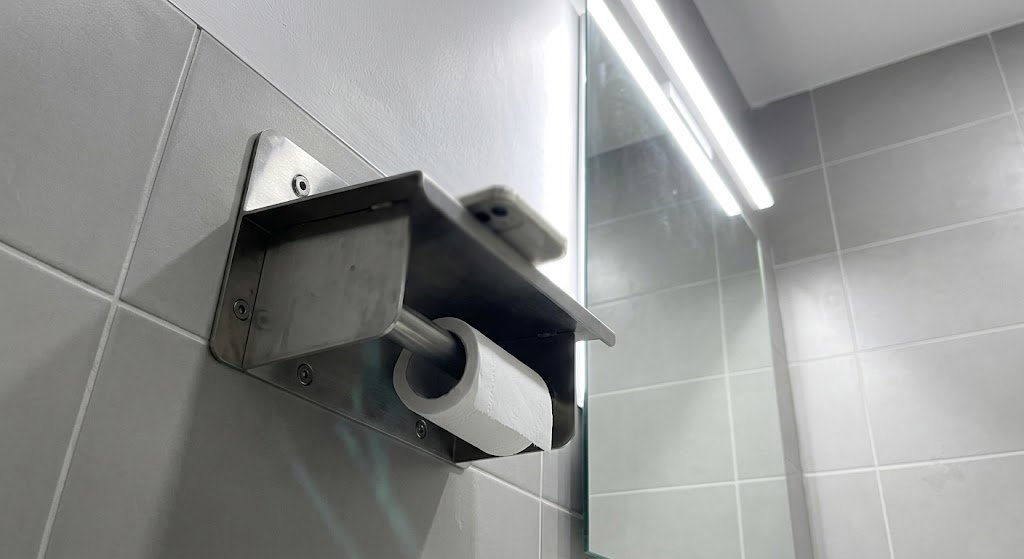 Hotel-Grade Anti-Theft Bathroom Fixture A hotel bathroom scene showing a sleek, wall-mounted toilet paper holder with a shelf, emphasizing its clean lines and secure, tamper-resistant mounting.
